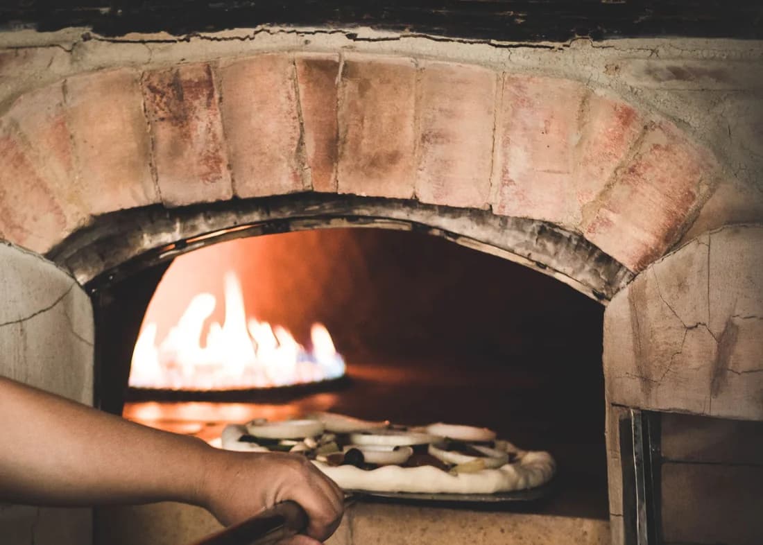 Una pizza entrando con la pala en la boca de un horno de leña encendido