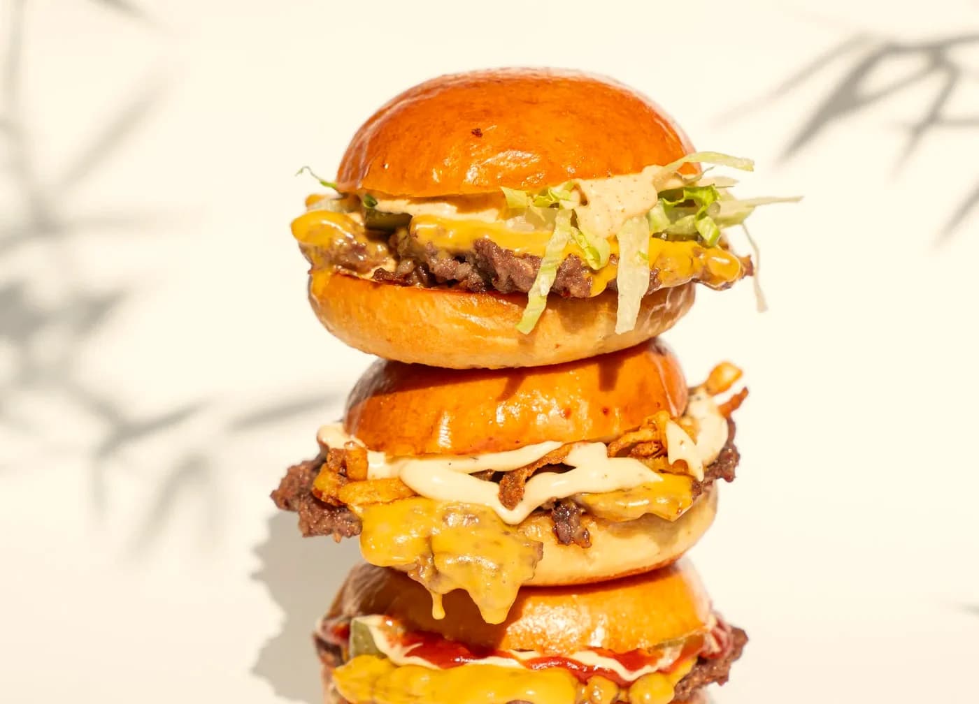 Tres hamburguesas dobles apiladas sobre fondo crema